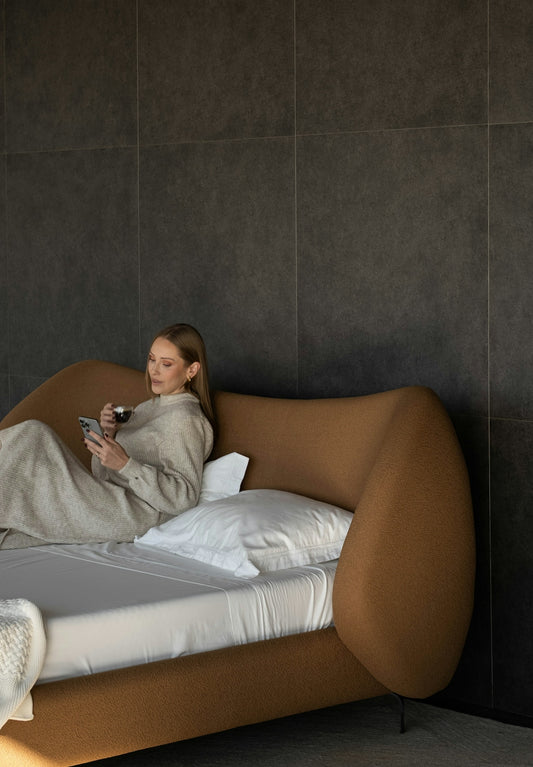 Woman in bed holding coffee and phone.
